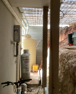 Photo showing an external model water heater and LP Gas cylindrs located at the back of a wall in an enclosed area.