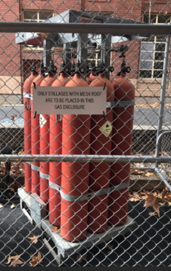 A photo of red gas cylinders behind a metal fence.