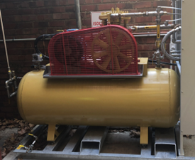 Photo shows a large gold canister connected to pipes, with a red fan on top.