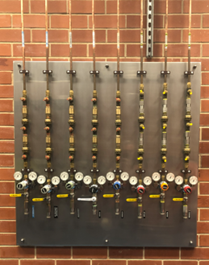 Photo of a gas connection station consisting of pipes and gauges, against a red brick wall.